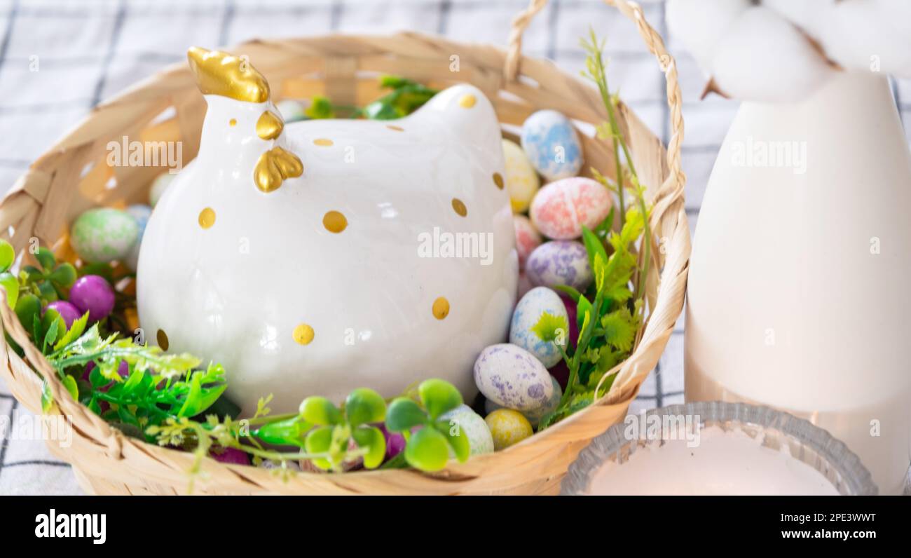 Decoración de Pascua de huevos de colores en una cesta y un pollo en la mesa de la cocina en un estilo rústico. Interior festivo de una casa de campo Foto de stock