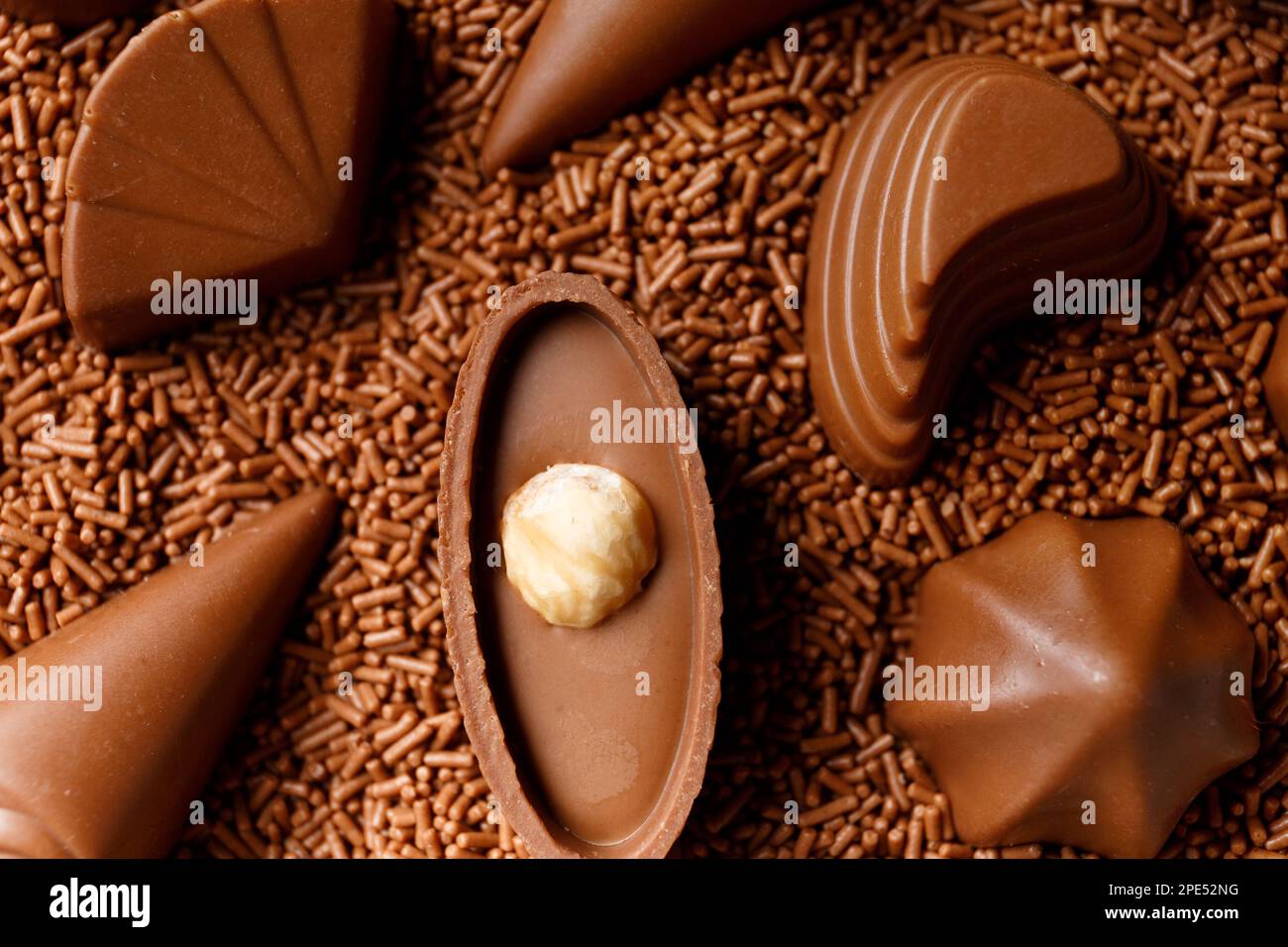 Dulces de chocolate negro bellamente formados sumergidos en chips de chocolate de cerca, concepto de fabricación de dulces de chocolate, fondo de chocolate. Foto de stock