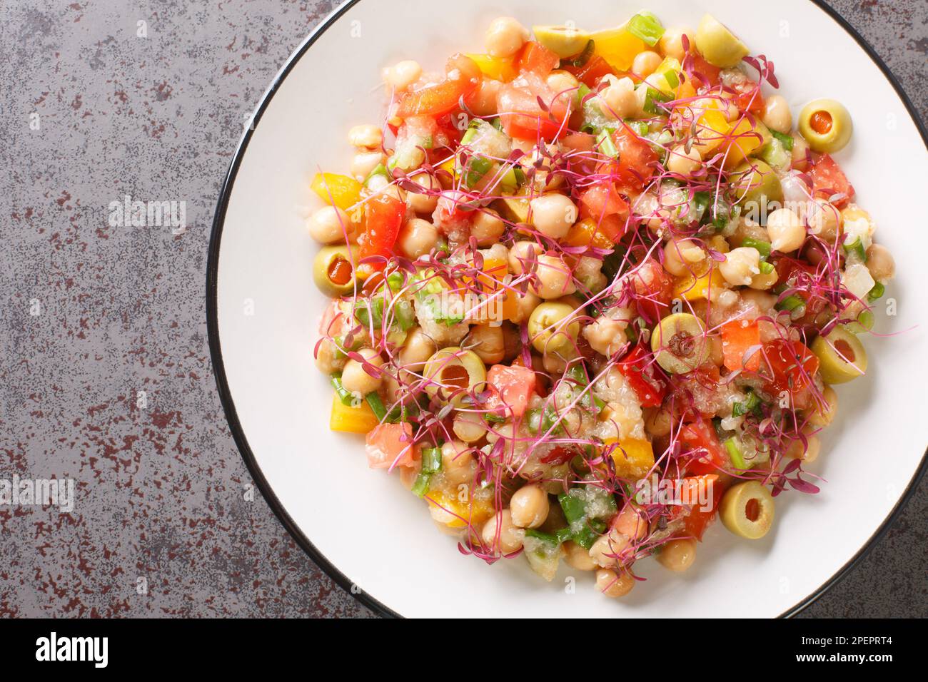 Ensalada de dieta mediterránea de garbanzos, pimientos, aceitunas, tomates, cebollas y amaranto microgreens y semillas de cerca en un plato sobre la mesa. Horizontal Foto de stock