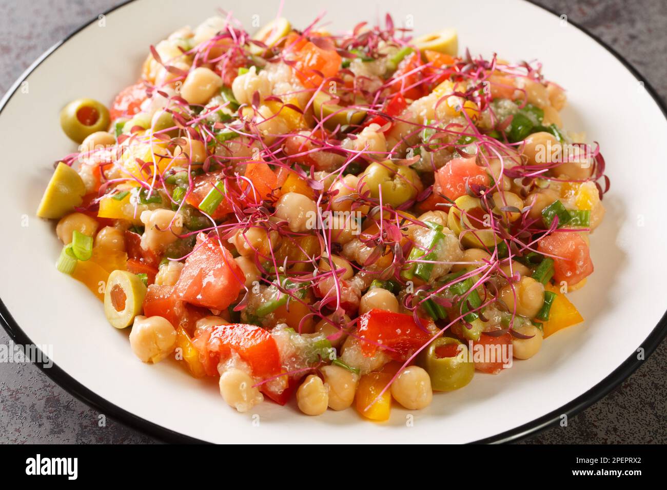 Ensalada de dieta mediterránea de garbanzos, pimientos, aceitunas, tomates, cebollas y amaranto microgreens y semillas de cerca en un plato sobre la mesa. Horizontal Foto de stock