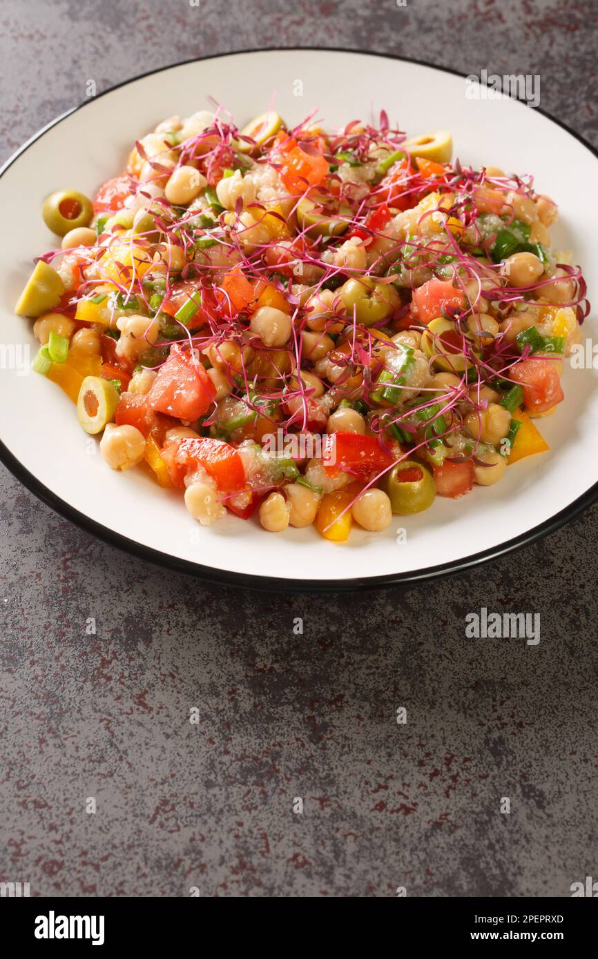 Ensalada dietética de garbanzos, pimientos, aceitunas, tomates, cebollas y amaranto microverde primer plano en un plato sobre la mesa. Vertical Foto de stock