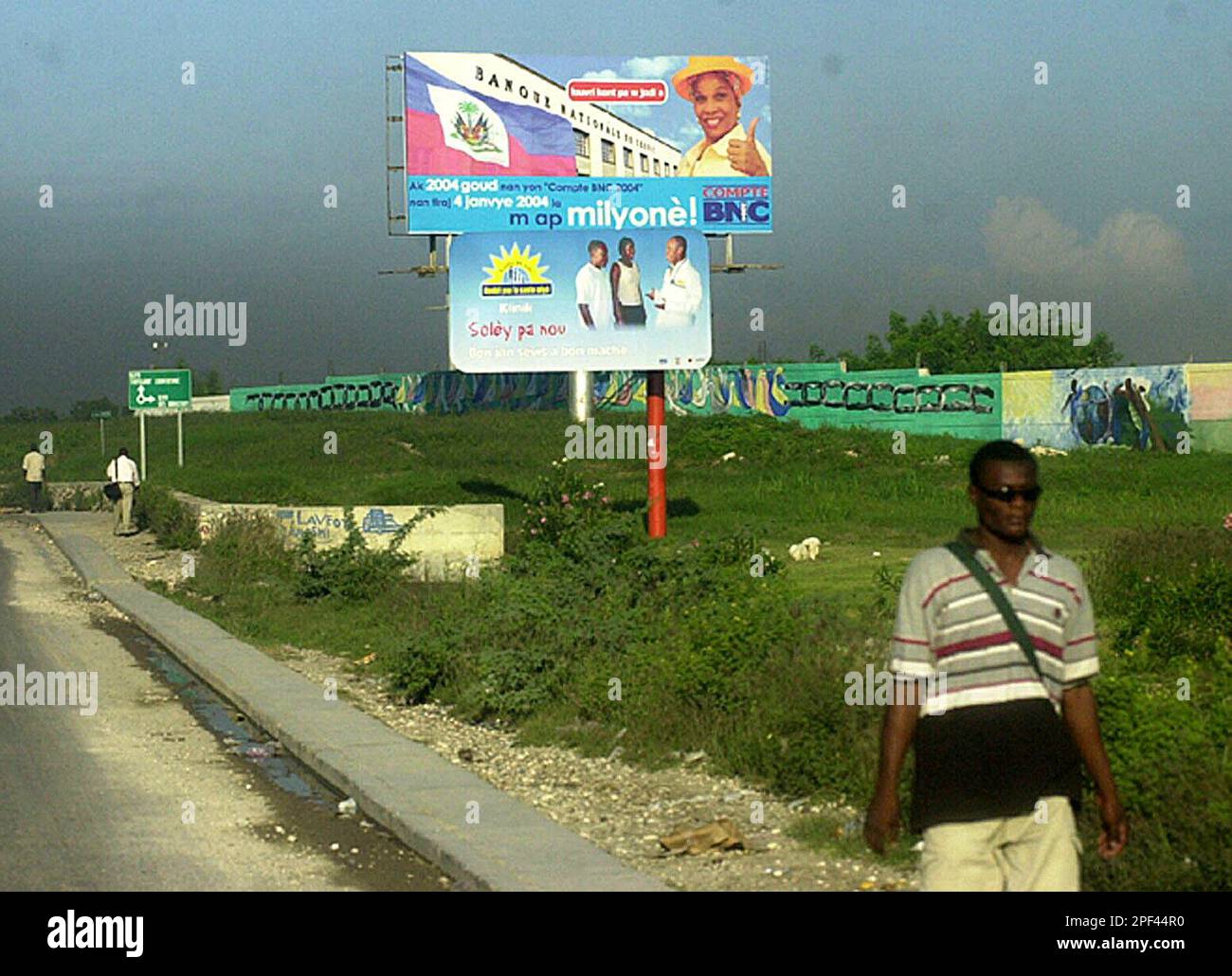 A Man Walks By Billboards Written In Creole Which Advertize A a-man-walks-by-billboards-written-in-creole-which-advertize-a