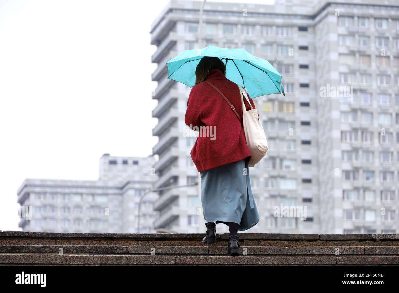 Mujer con paraguas que sube los pasos en el fondo de los edificios de la ciudad. Lluvia en la ciudad de primavera Foto de stock