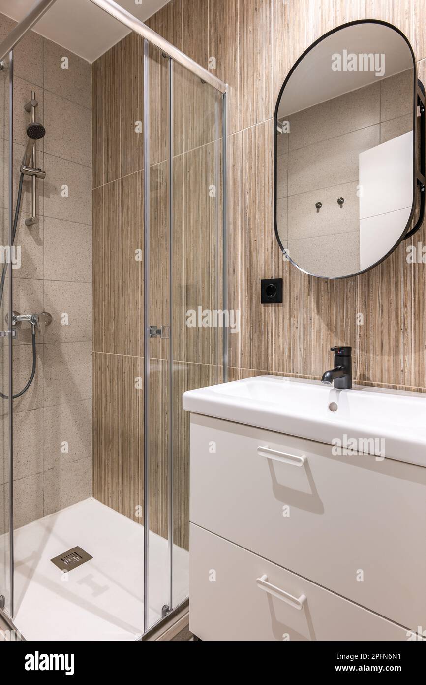 Primer plano de un pequeño cuarto de baño con un moderno gabinete de ducha  de vidrio blanco y un lavabo de cerámica con grifo negro y elegantes  azulejos beige. Concepto de baño