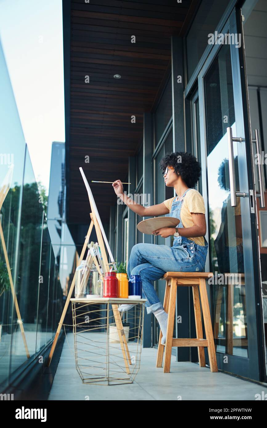 Tómese un tiempo para sentarse y ponerse artístico. un joven artista pintando en un lienzo mientras se sienta en el balcón en casa. Foto de stock