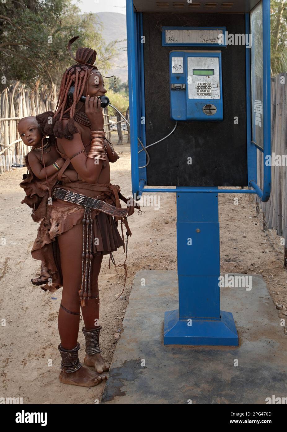 Una mujer Himba, la señorita Mukamuhuvare, habla con un amigo en un teléfono público en un pueblo en el río Kunene. Foto de stock