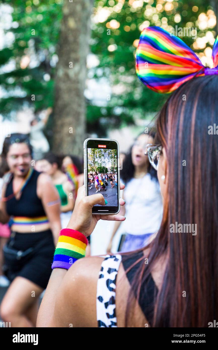 Mujer vestida con la bandera del orgullo con un teléfono móvil en la mano. Redes sociales. Fotos y videos en el festival del orgullo. Foto de stock