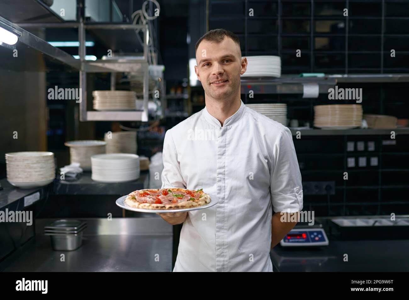 Retrato de pizzaiolo masculino presentando pizza recién cocinada Foto de stock