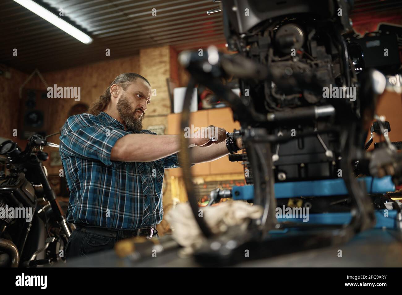 Motociclista masculino concentrado que sirve su motocicleta en el taller de garaje Foto de stock