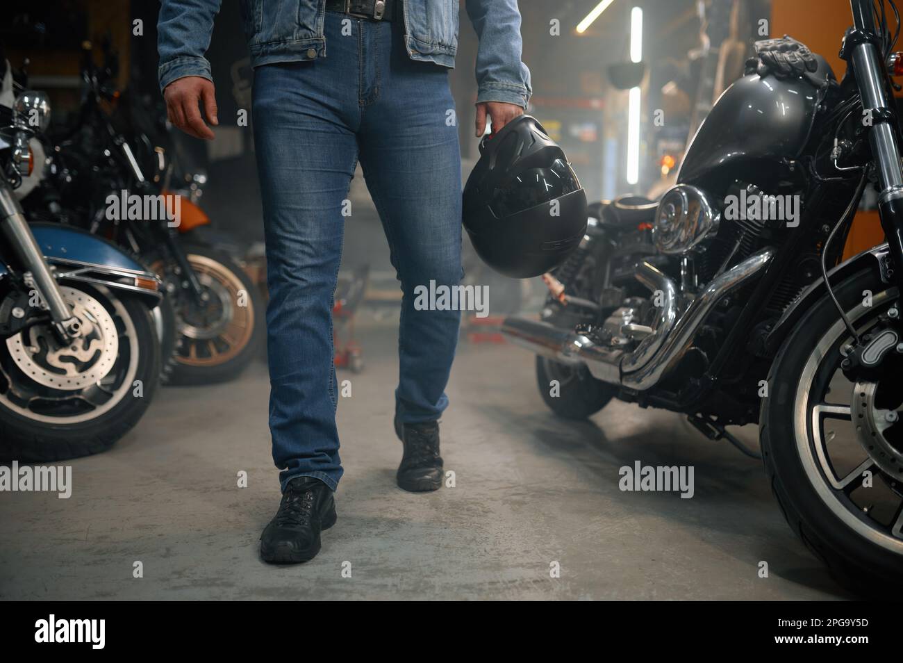 Tiro recortado de motorista llevando casco de pie sobre la fila de la motocicleta en el garaje Foto de stock