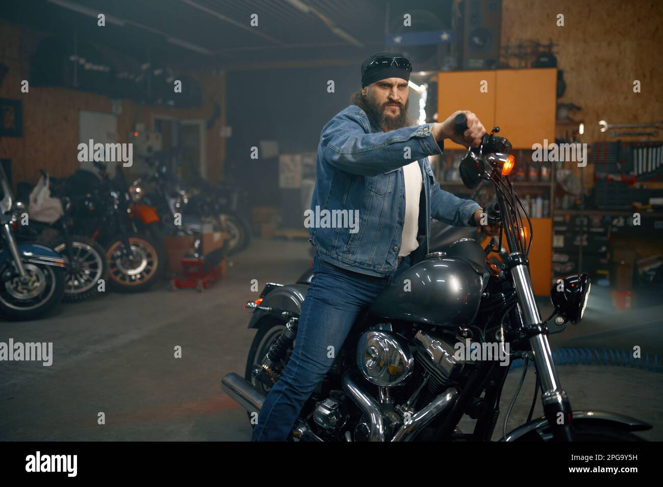 Hombre barbudo guapo probando nueva moto en tienda de garaje Foto de stock