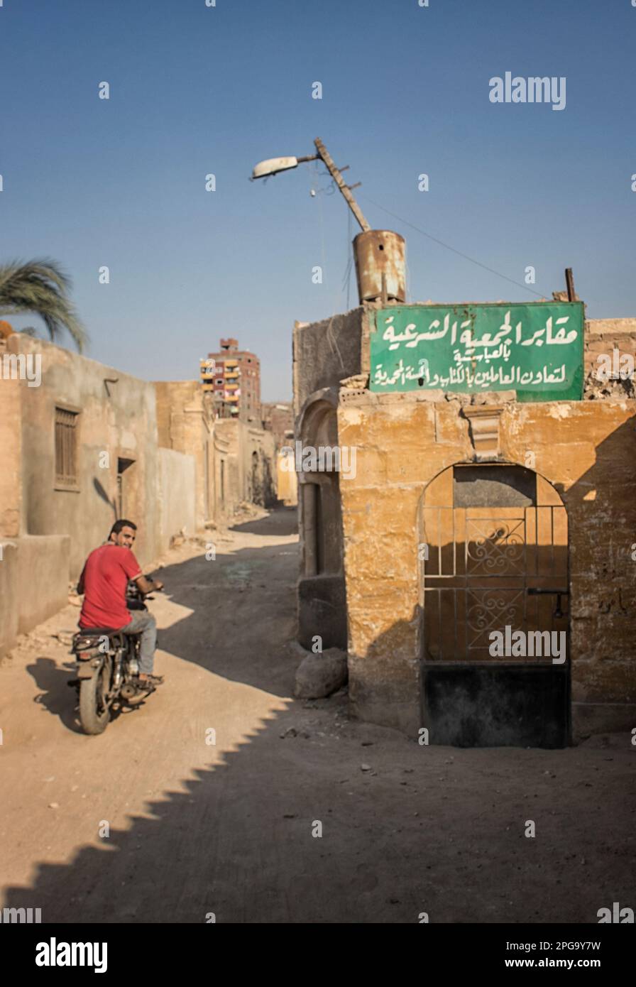 Hombre en una motocicleta que sale de la ciudad de los muertos. La Ciudad de los Muertos, o Necrópolis de El Cairo, también conocida como el Qarafa es una serie de vastas necrópolis y cementerios de la era islámica en El Cairo, Egipto. Foto de stock