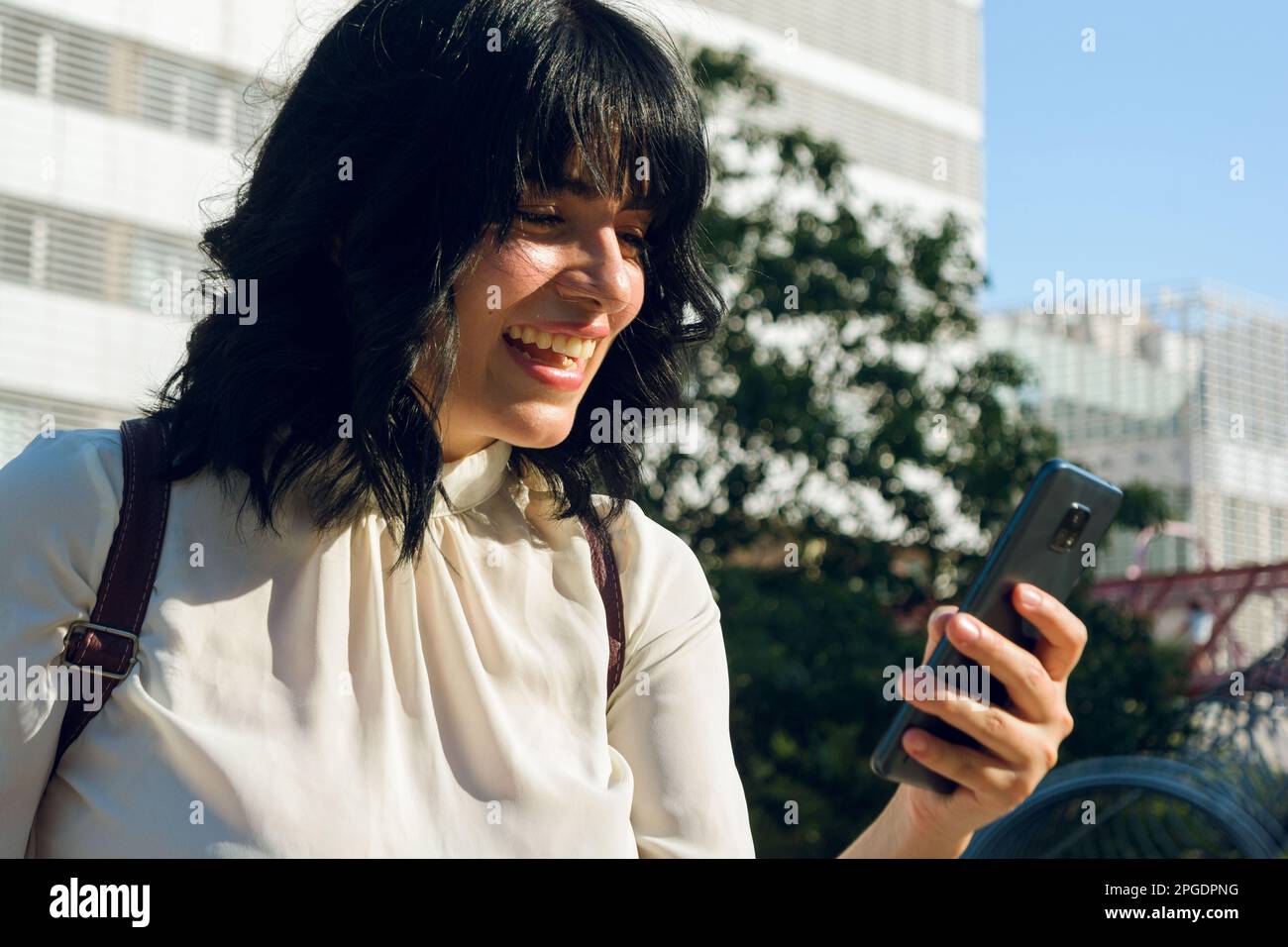 felicidad y tranquilidad para pasar las pruebas universitarias, mujer latina al aire libre sonriendo y usando el teléfono, concepto de tecnología, espacio de copia. Foto de stock