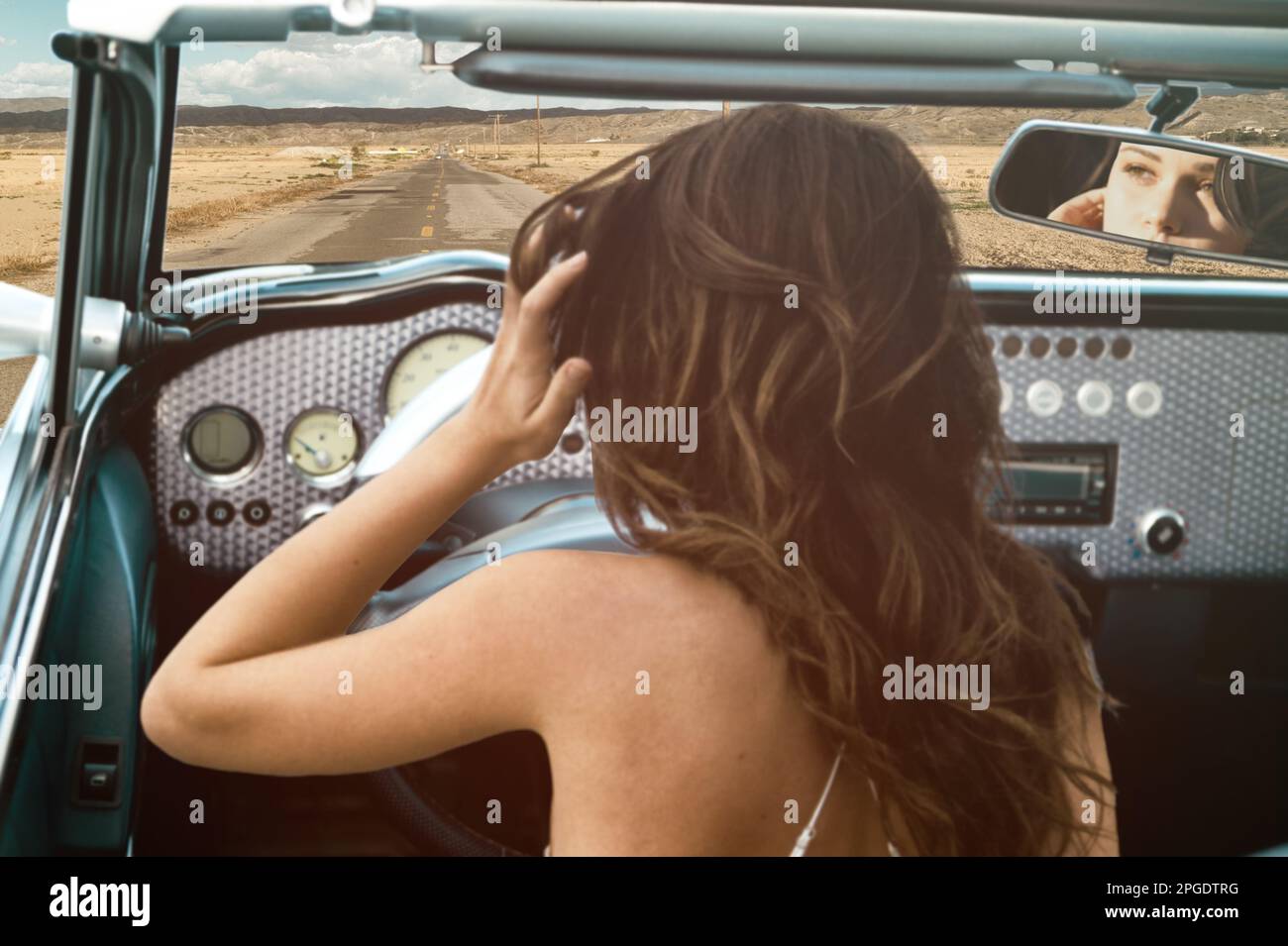 Vista trasera de una mujer joven en un viaje por carretera en un coche convertible vintage, San Bernardino, California, EE.UU Foto de stock