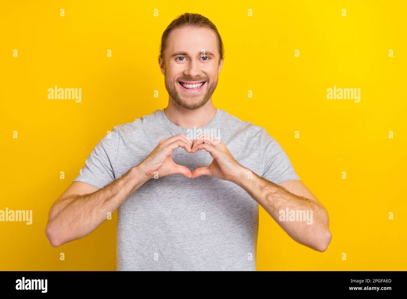 Foto de hombre divertido alegre usa camiseta gris sonriendo mostrando dedos  corazón aislado fondo de color amarillo Fotografía de stock - Alamy