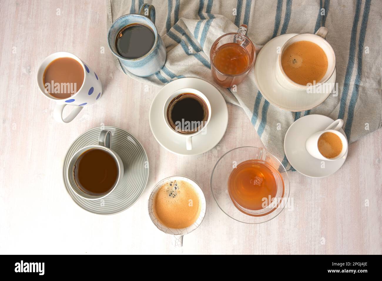 Varias tazas y tazas diferentes con bebidas de café y té en una mesa ligera  con una toalla azul gris, vista de ángulo alto desde arriba, enfoque  seleccionado, estrecho Fotografía de stock -