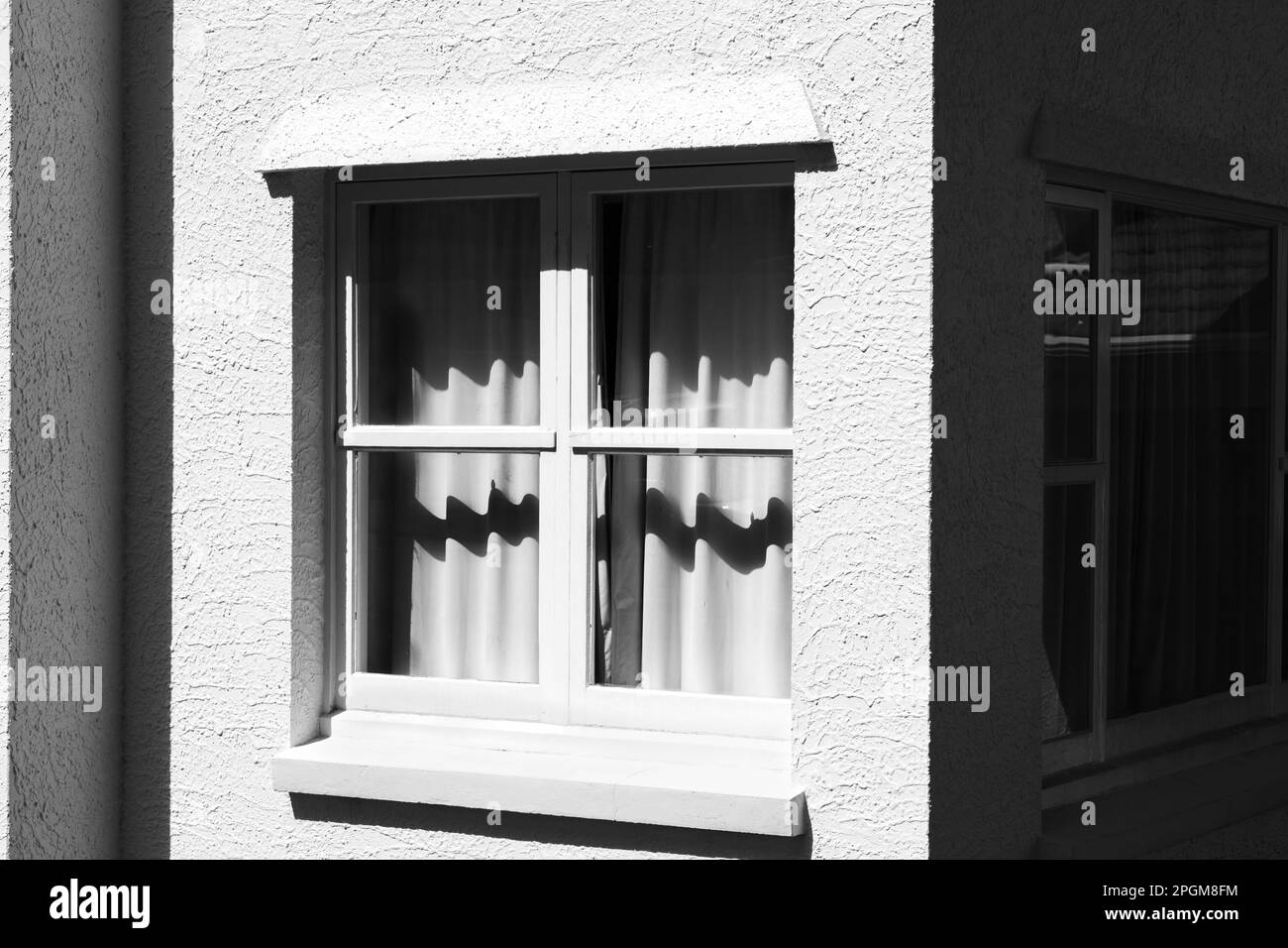 Exterior de estuco y ventanas con marco de madera con sombras en cortinas blancas Foto de stock