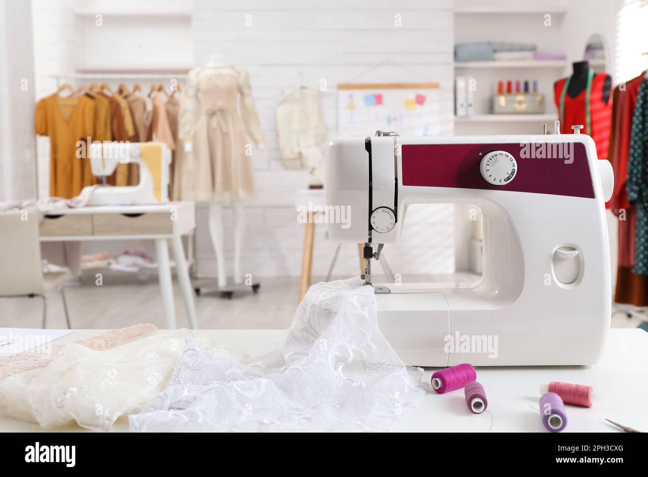 Máquina de coser moderna con tela e hilos brillantes en la mesa en taller  de confección Fotografía de stock - Alamy