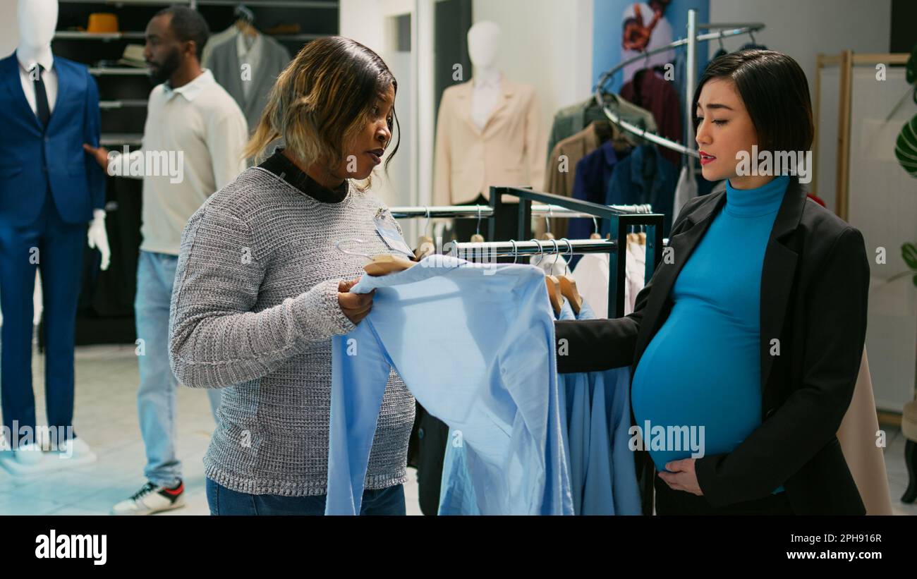 Mujer asiática con la compra del bache del bebé para la ropa en los grandes  almacenes en el centro comercial, mirando nuevas marcas de moda en perchas.  Futura madre joven que está