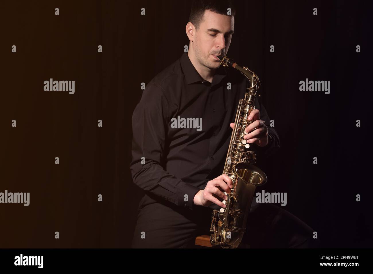 Hombre joven jugando saxofón sobre fondo oscuro. Espacio para texto Foto de stock