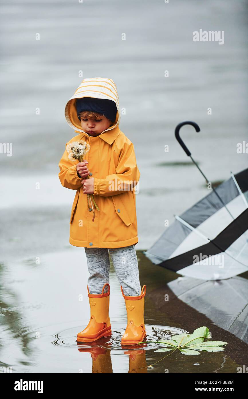 niño con capa impermeable amarilla, botas y paraguas jugando al