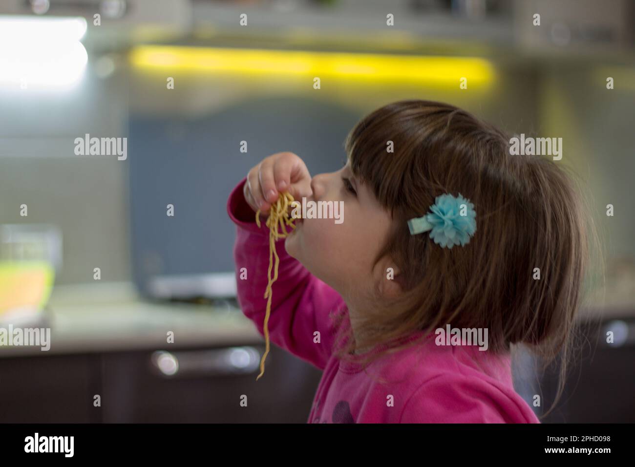 Imagen de una adorable niña morena comiendo espaguetis con sus manos. Foto de stock