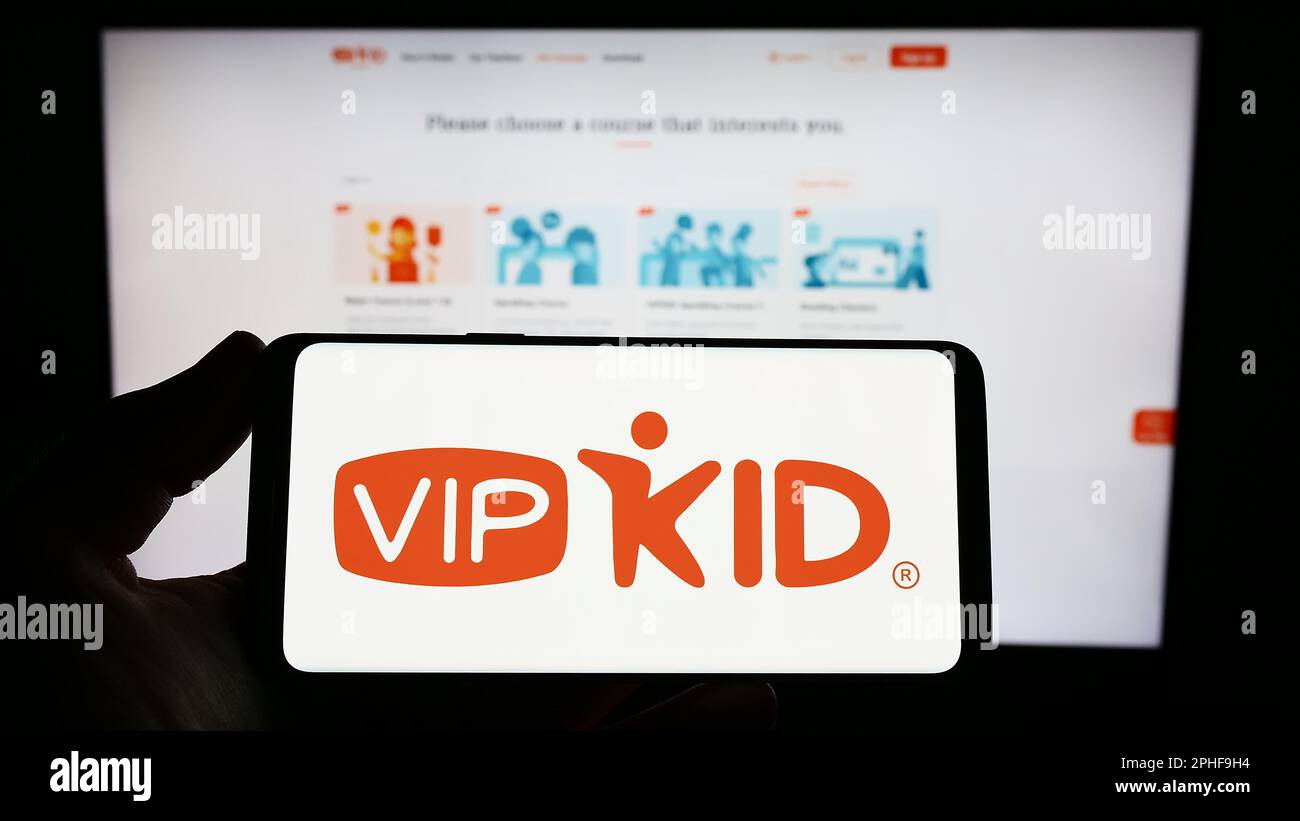 Persona que sostiene el smartphone con el logotipo de la empresa de e-learning VIPKid en la pantalla delante del sitio web. Enfoque en la pantalla del teléfono. Foto de stock