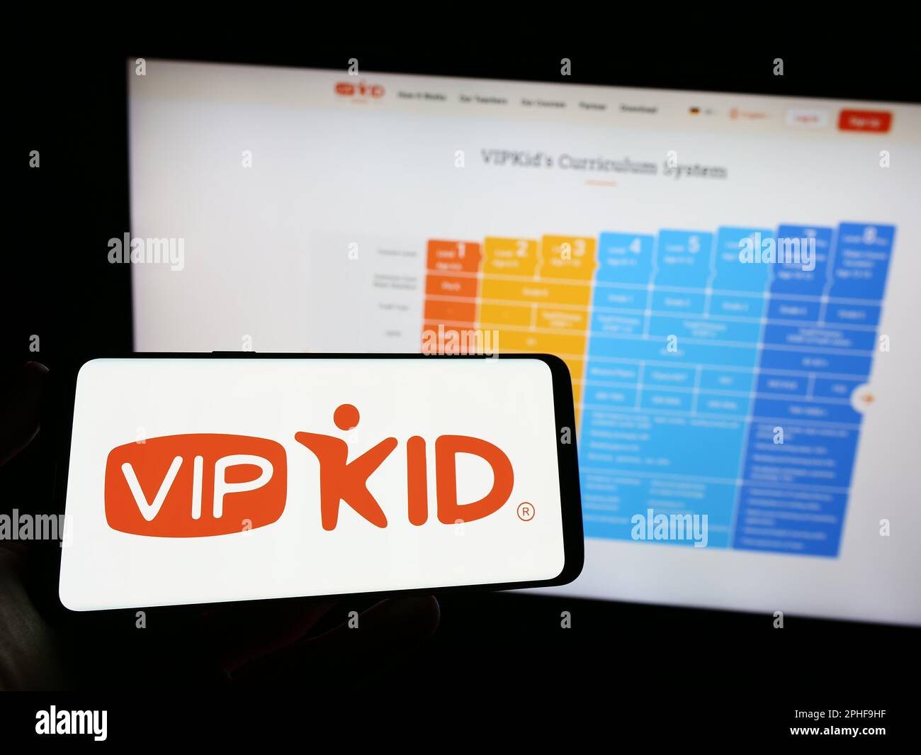 Persona que sostiene el teléfono móvil con el logotipo de la compañía de e-learning VIPKid en la pantalla delante de la página web del negocio. Enfoque en la pantalla del teléfono. Foto de stock