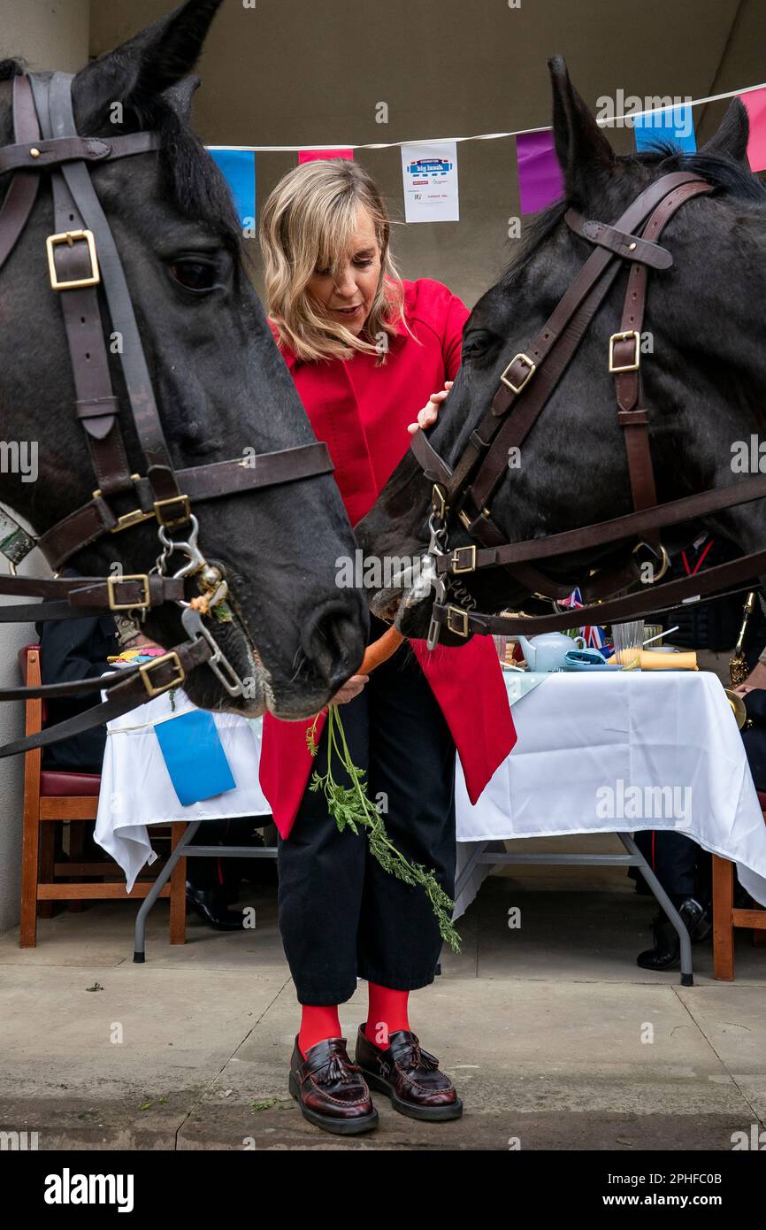 El presentador Mel Geidroyc alimenta una zanahoria a los caballos Hastings y Warrior de la caballería doméstica durante el Gran Almuerzo de Coronación con militares en Wellington Barracks, Londres. Fecha de la fotografía: Martes 28 de marzo de 2023. Foto de stock