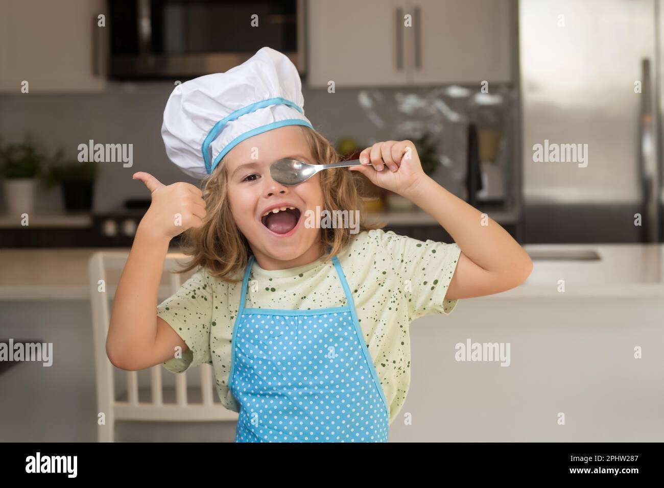 Divertido cocinero niño pequeño usando gorro uniforme de cocina y delantal  de comida cocida en la cocina. Los niños están preparando la masa,  cocinando galletas en la cocina Fotografía de stock 