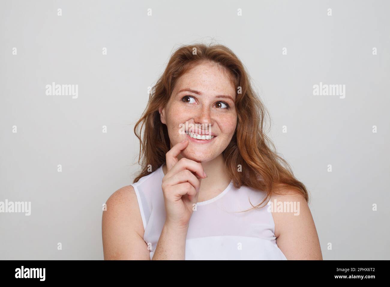Retrato de mujer pelirroja alegre pensando mirando hacia arriba y sonriendo sobre fondo blanco Foto de stock