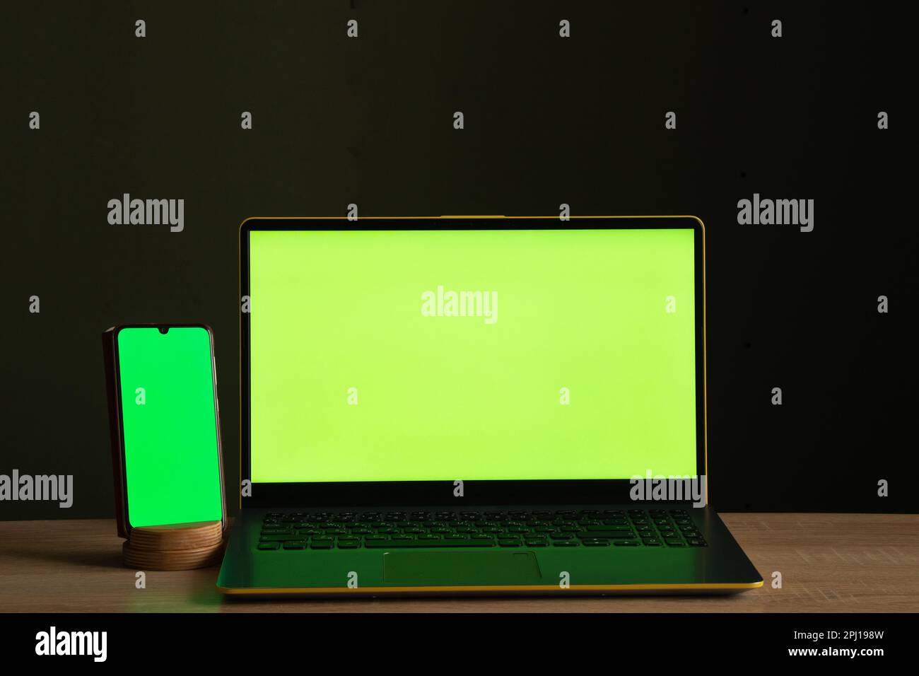 una computadora portátil con una pantalla verde y un teléfono táctil está sobre la mesa Foto de stock