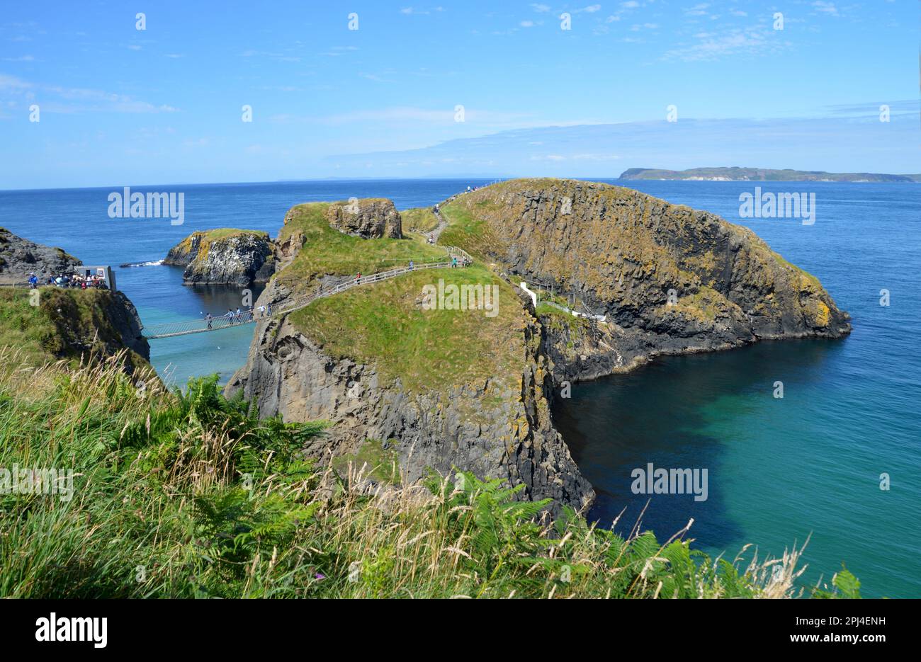 Irlanda del Norte, Condado de Antrim, Costa de la Calzada: El puente de cuerda que conecta la isla de Carrick-a-Rede (derecha) con el continente, con la isla de Rathlin en Th Foto de stock