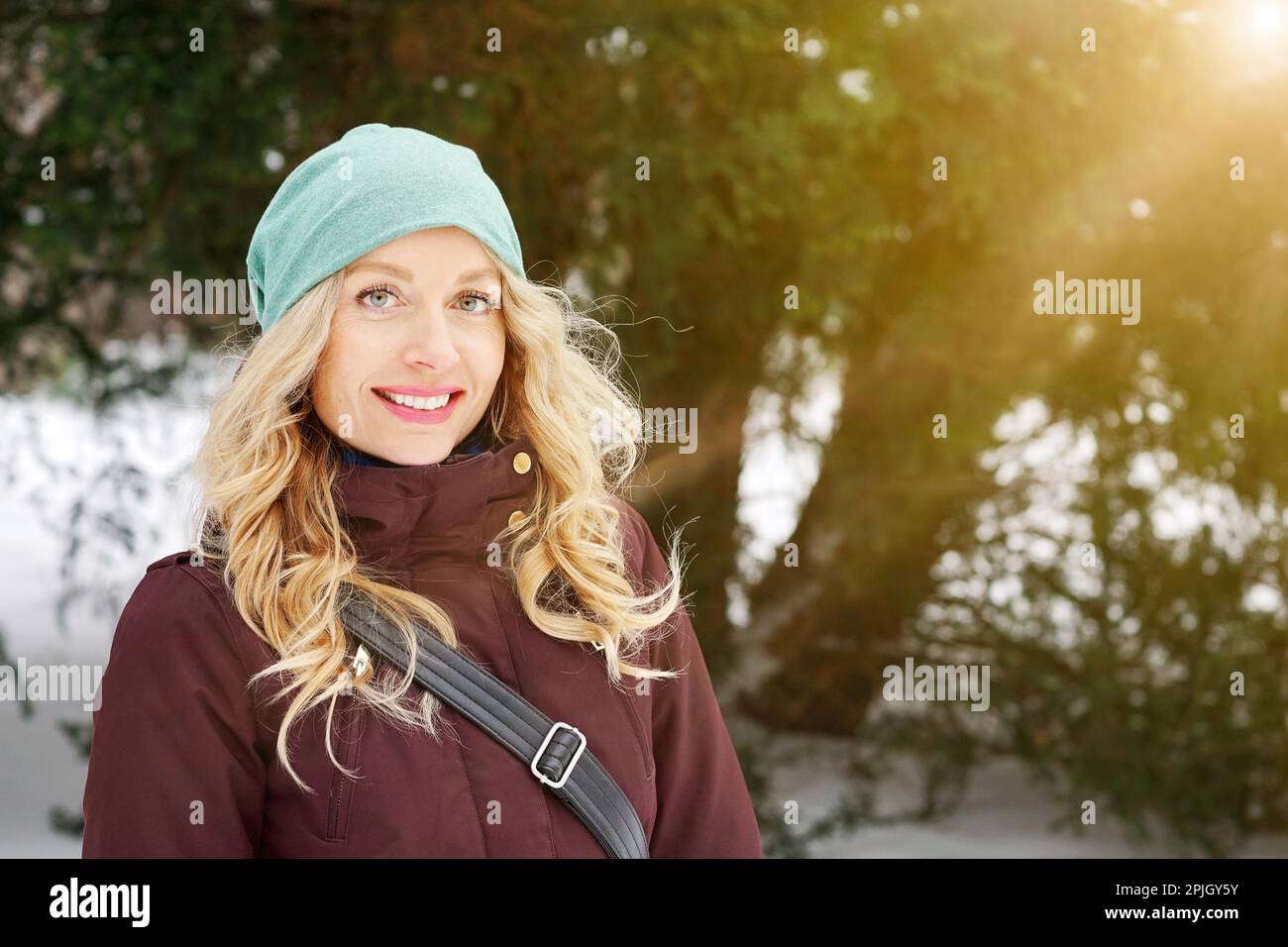 mujer rubia con ropa cálida de invierno y sombrero de punto disfrutando de un día soleado en invierno, con luz de escape llamarada al sol Foto de stock