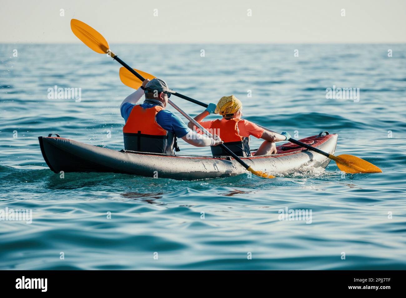 Feliz pareja kayaks en un kayak inflable en el mar al atardecer. Pareja  kanoeing en el mar cerca de la isla con montañas. Gente en kayak en la vida  Fotografía de stock -