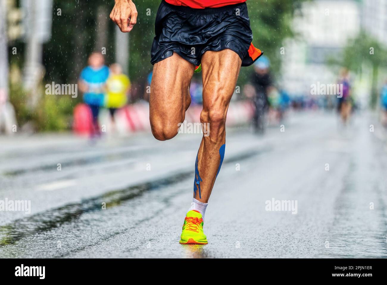 close-up musculosas piernas corredor masculino que corre la carrera de la ciudad del maratón, atleta corre sobre asfalto mojado después de la lluvia Foto de stock