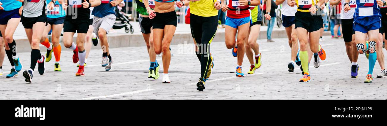 los corredores masculinos y femeninos de grupo grande corren una carrera de maratón en la ciudad en adoquines Foto de stock