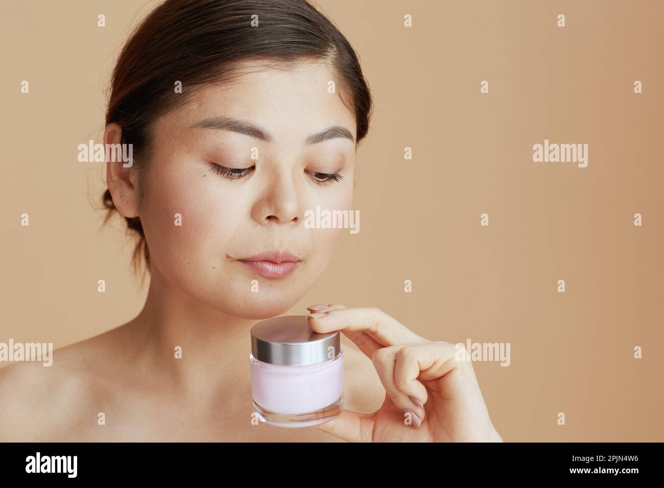 mujer asiática moderna con tarro de crema facial sobre fondo beige. Foto de stock