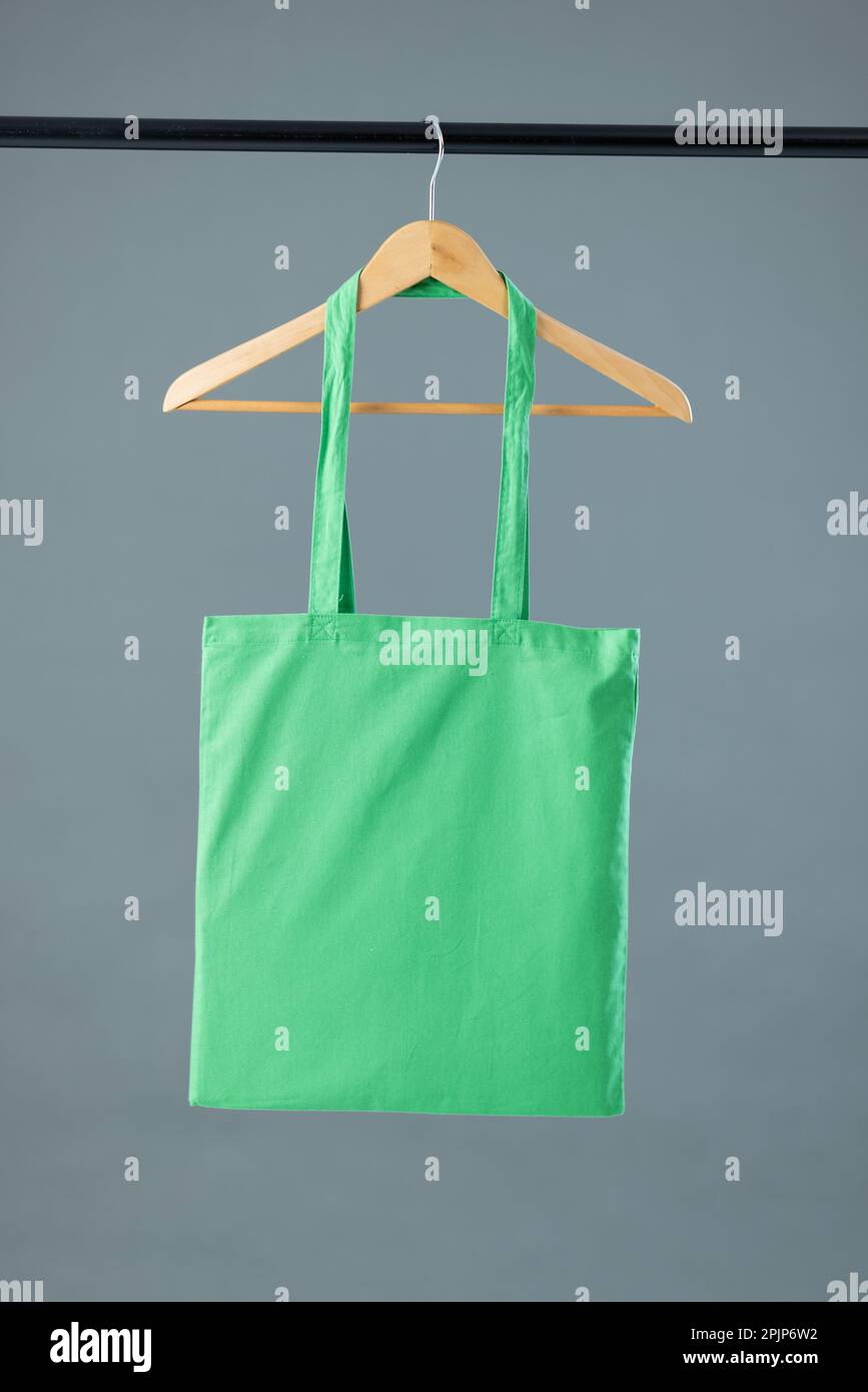 Cierre de la bolsa de lona verde que cuelga en la percha de ropa de madera  con espacio de copia sobre fondo gris. Eco amistoso bolsas de compras y  concepto de moda