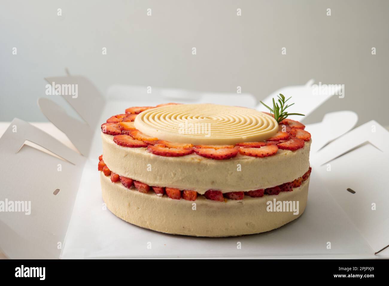 Pastel de cumpleaños vegano con vainilla y fresa cubierto con chocolate  blanco en una caja de cartón abierta sobre una mesa y un fondo blanco  Fotografía de stock - Alamy