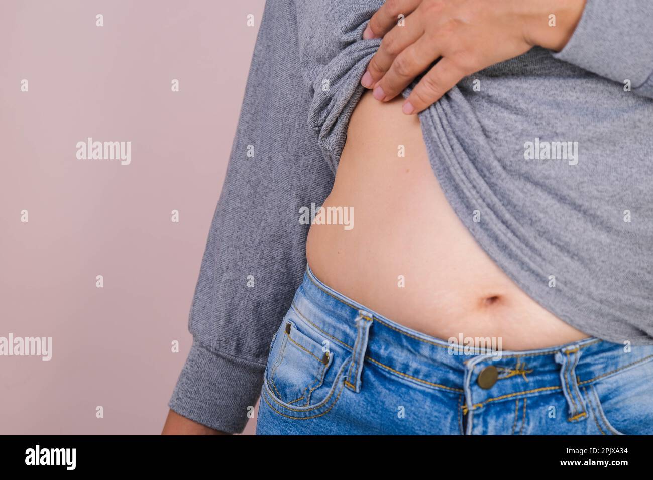 Mano gorda de la mujer que sostiene la grasa excesiva del vientre aislada sobre fondo rosado. Vientre graso con sobrepeso de la mujer. Dieta femenina y concepto de cuidado de la salud del cuerpo Foto de stock