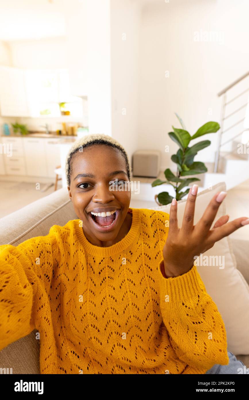 Mujer joven afroamericana confundida con el pelo corto gritando y gesticulando mientras se sienta en el sofá Foto de stock