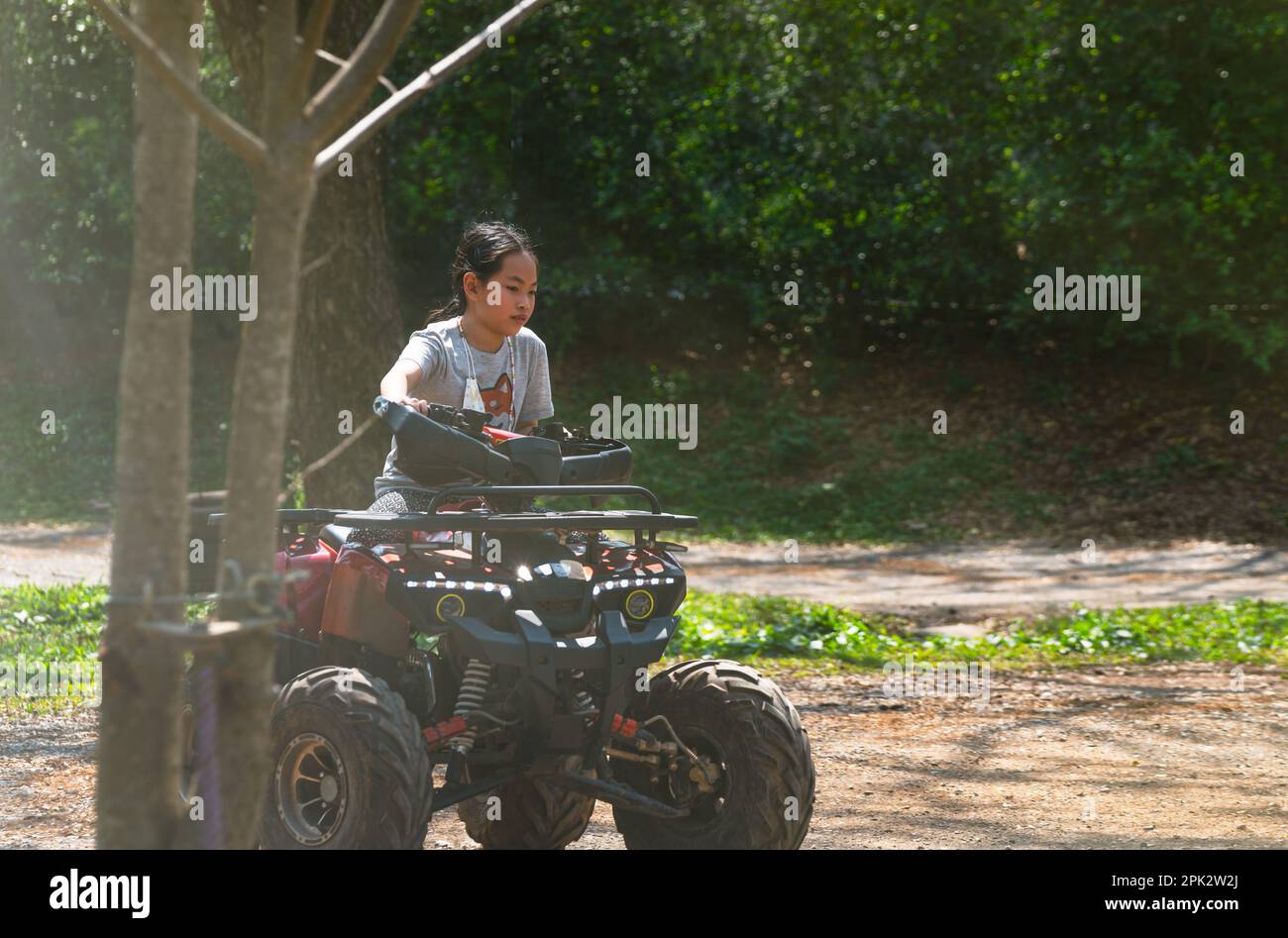 Niña asiática a los 9 años de edad por primera vez montando una moto ATV por sí misma, montando en la pista de campo ATV bajo la luz del sol, actividad al aire libre Foto de stock