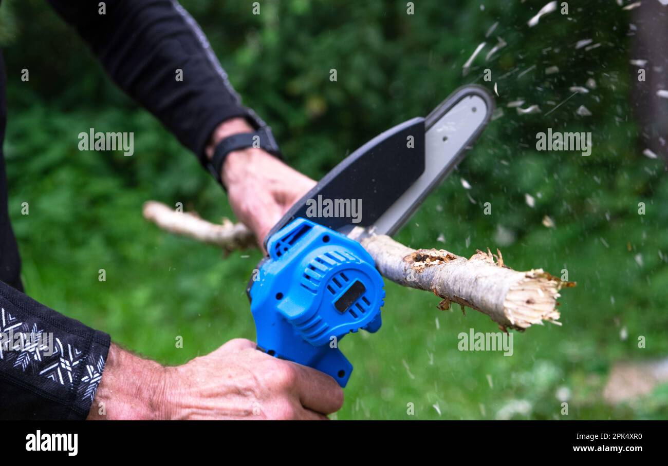 Sierra eléctrica portátil portátil portátil de mano en una batería para  cortar leña y madera. Primer plano, una mano aserrando un tronco, astillas  volando Fotografía de stock - Alamy