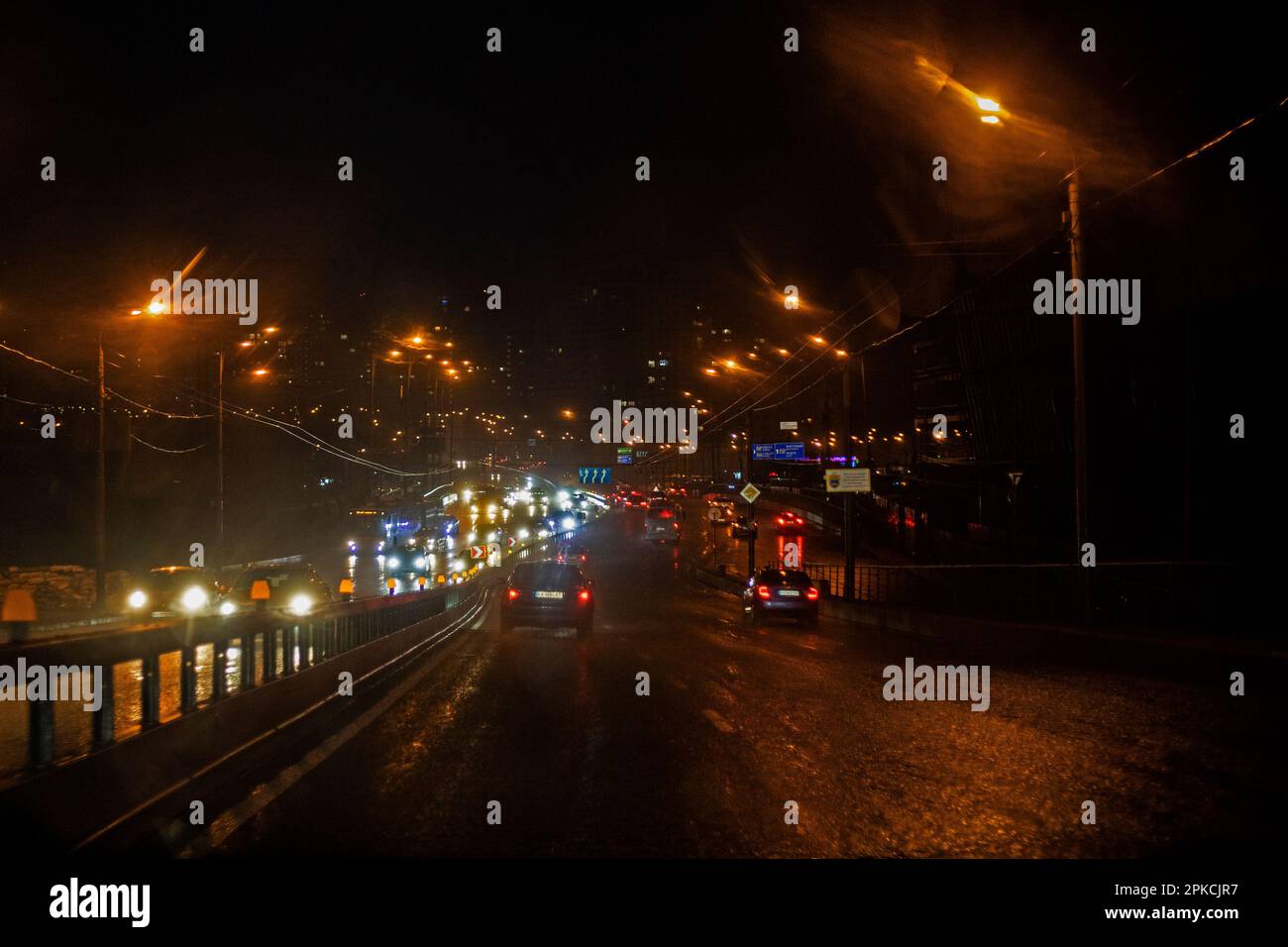 carretera húmeda nocturna en la ciudad iluminada por la luz amarilla de las linternas bajo la lluvia. Mal tiempo Foto de stock