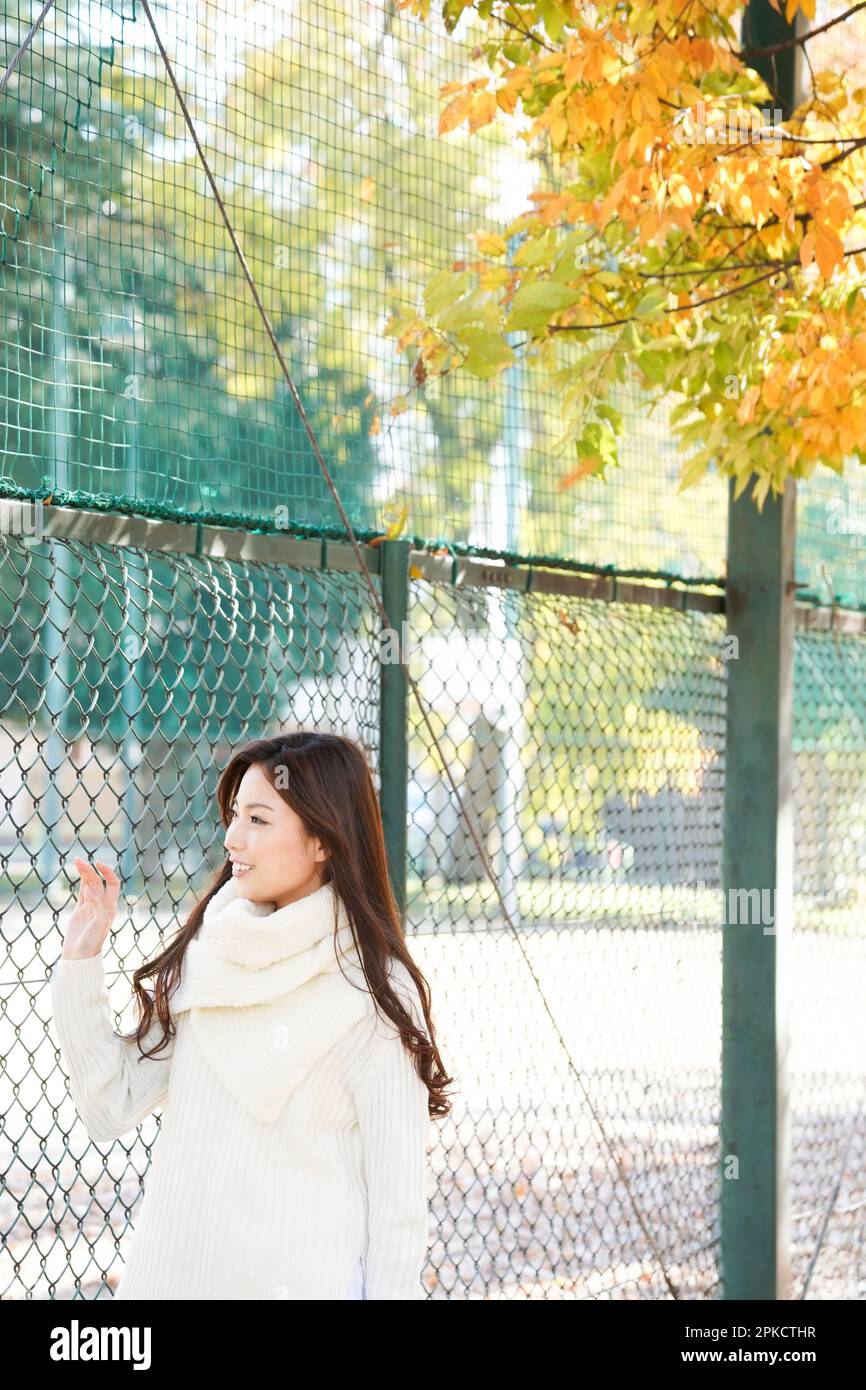 Una mujer de 20s años caminando frente a una valla de alambre en un parque a finales de otoño Foto de stock