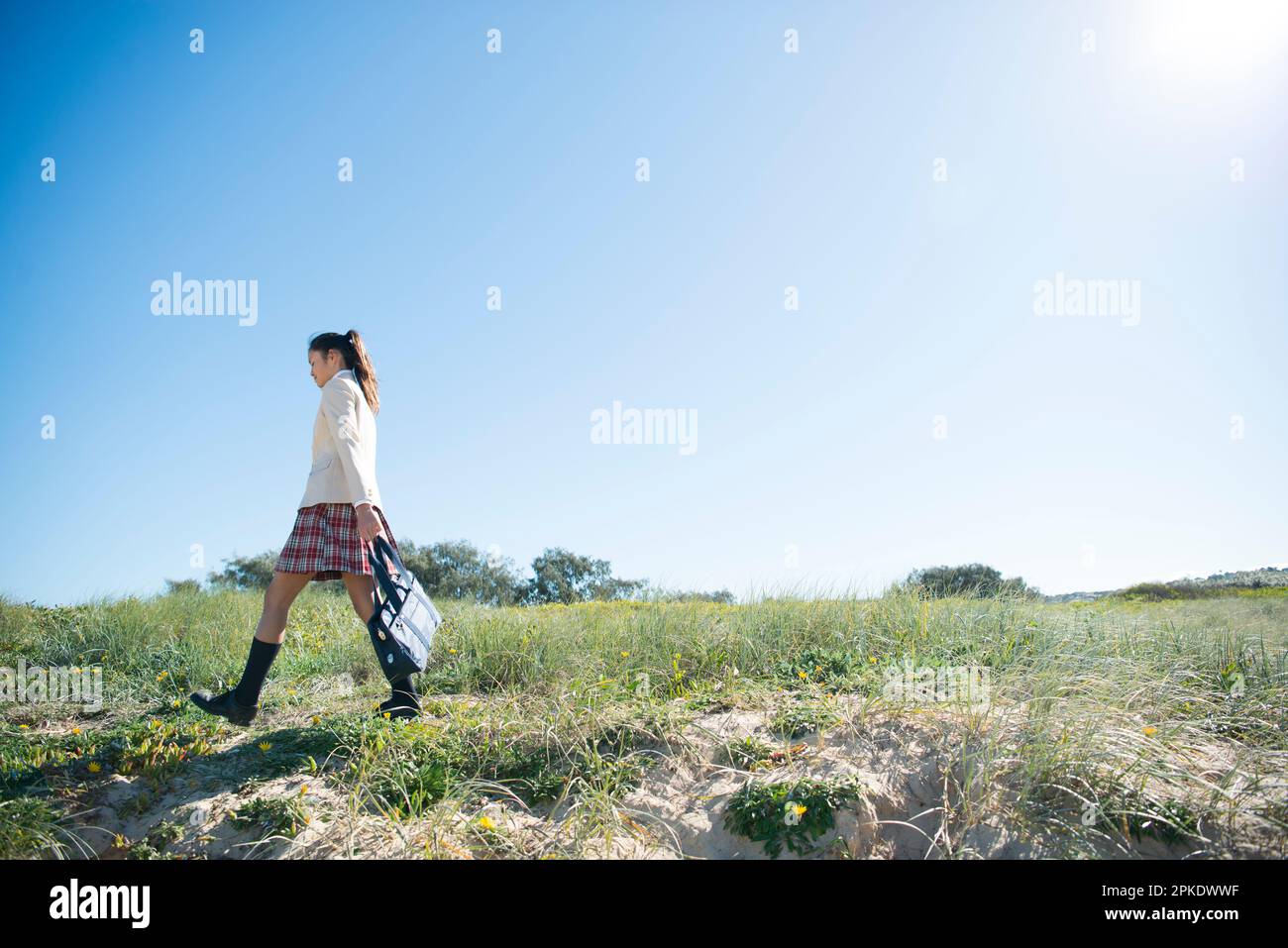 Colegiala en uniforme escolar caminando en un prado Foto de stock