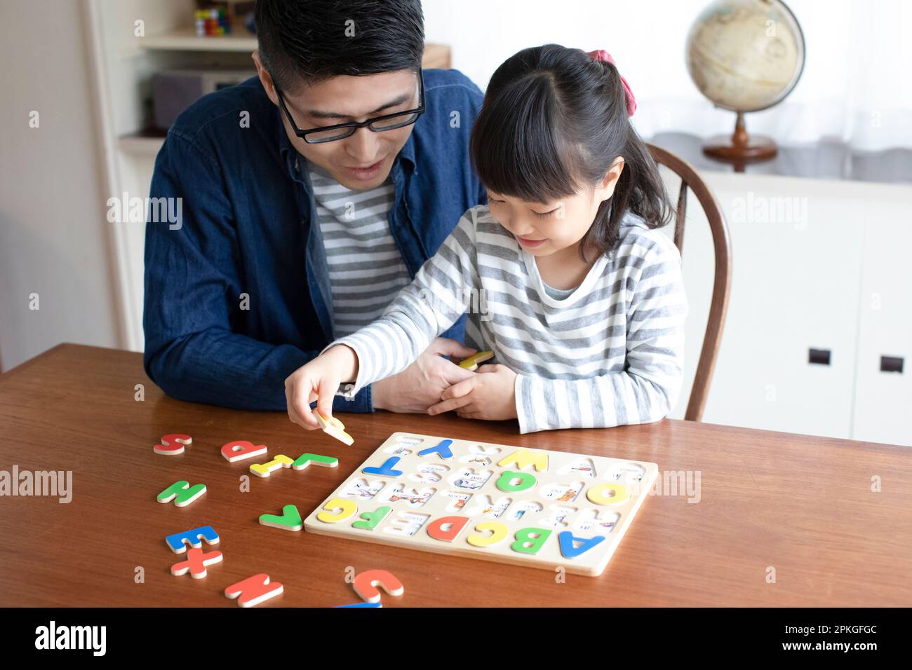 Chica haciendo rompecabezas del alfabeto y su padre ayudándola Foto de stock