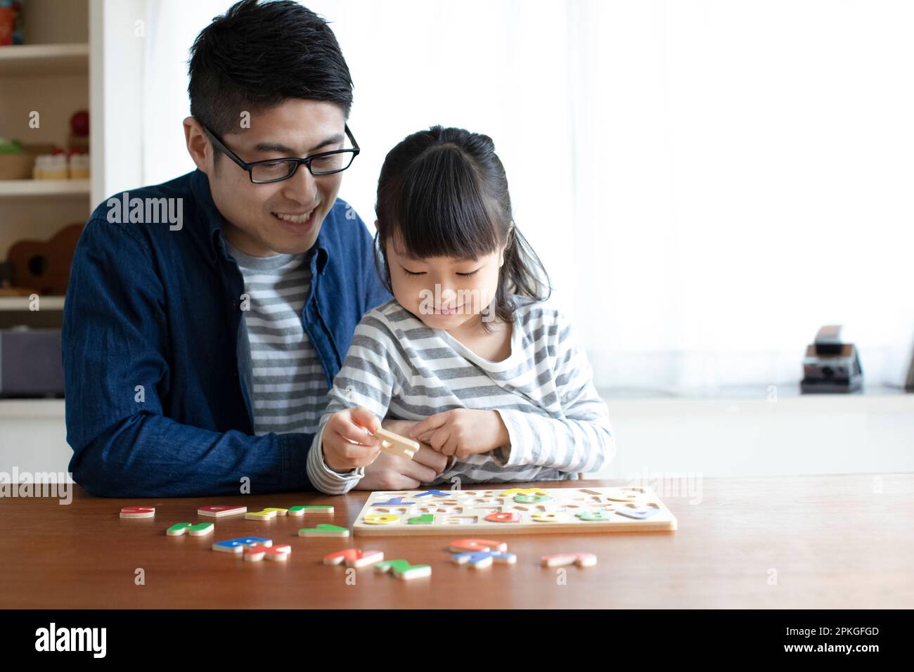 Chica haciendo rompecabezas del alfabeto y su padre ayudándola Foto de stock