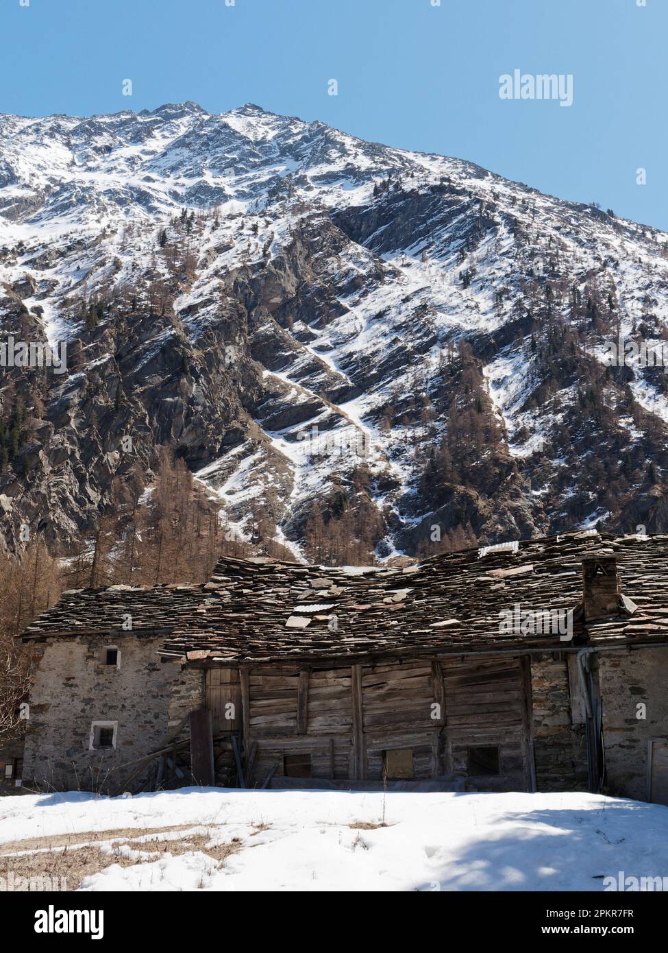 Edificio tradicional de madera bajo una montaña cubierta de nieve en Valnoney en el Parque Nacional Gran Paradiso, Valle de Aosta, Italia Foto de stock